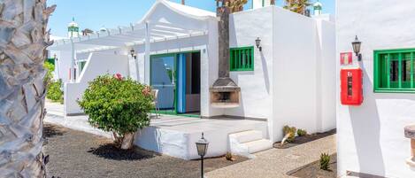 A white building with green shutters, a small garden, and a traditional stove.