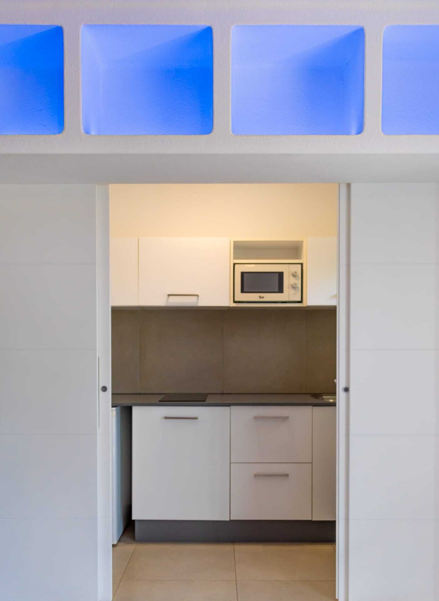 Una cocina compacta con armarios blancos, microondas y una pequeña encimera.