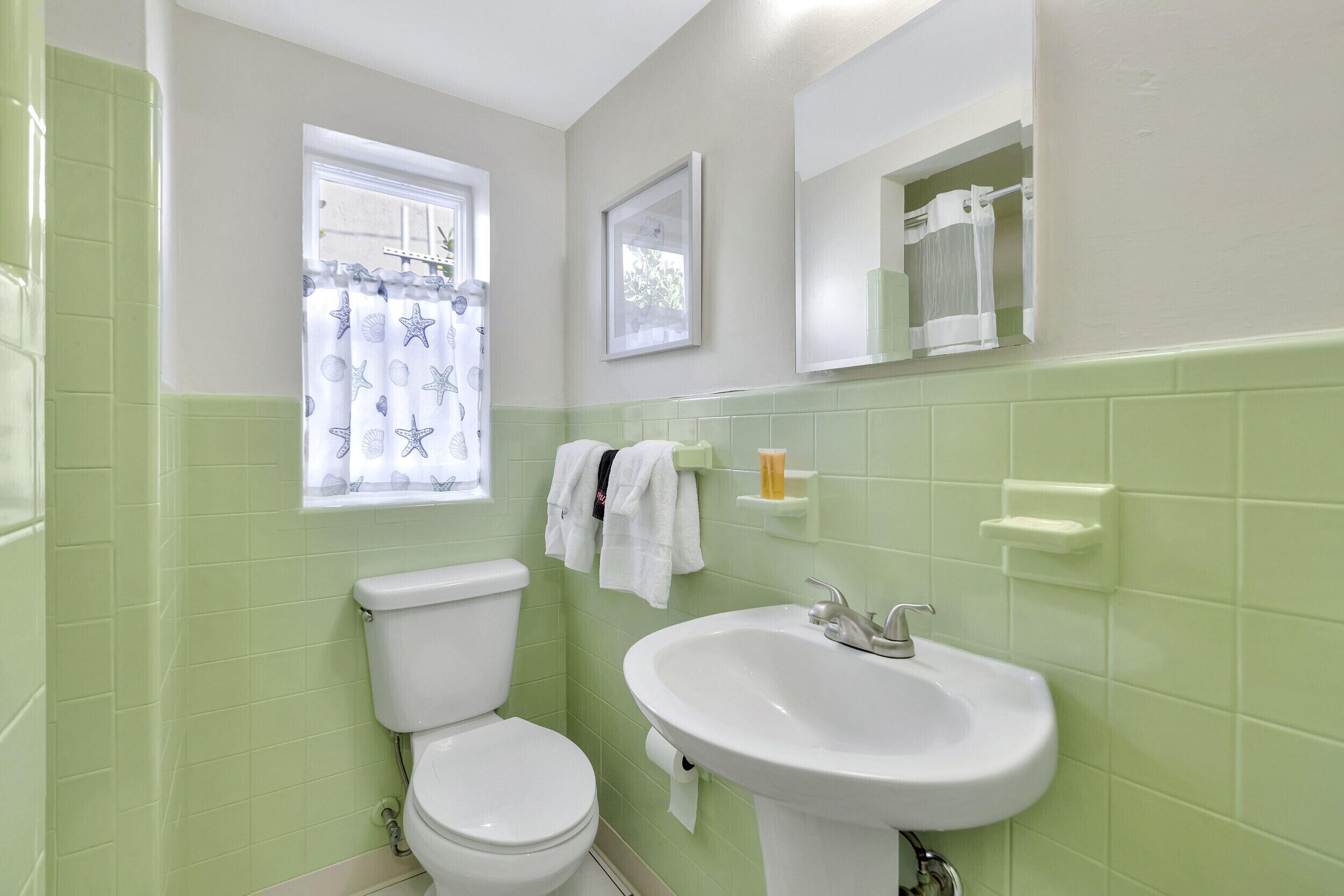 Un baño con inodoro, lavabo y ventana con cortina.