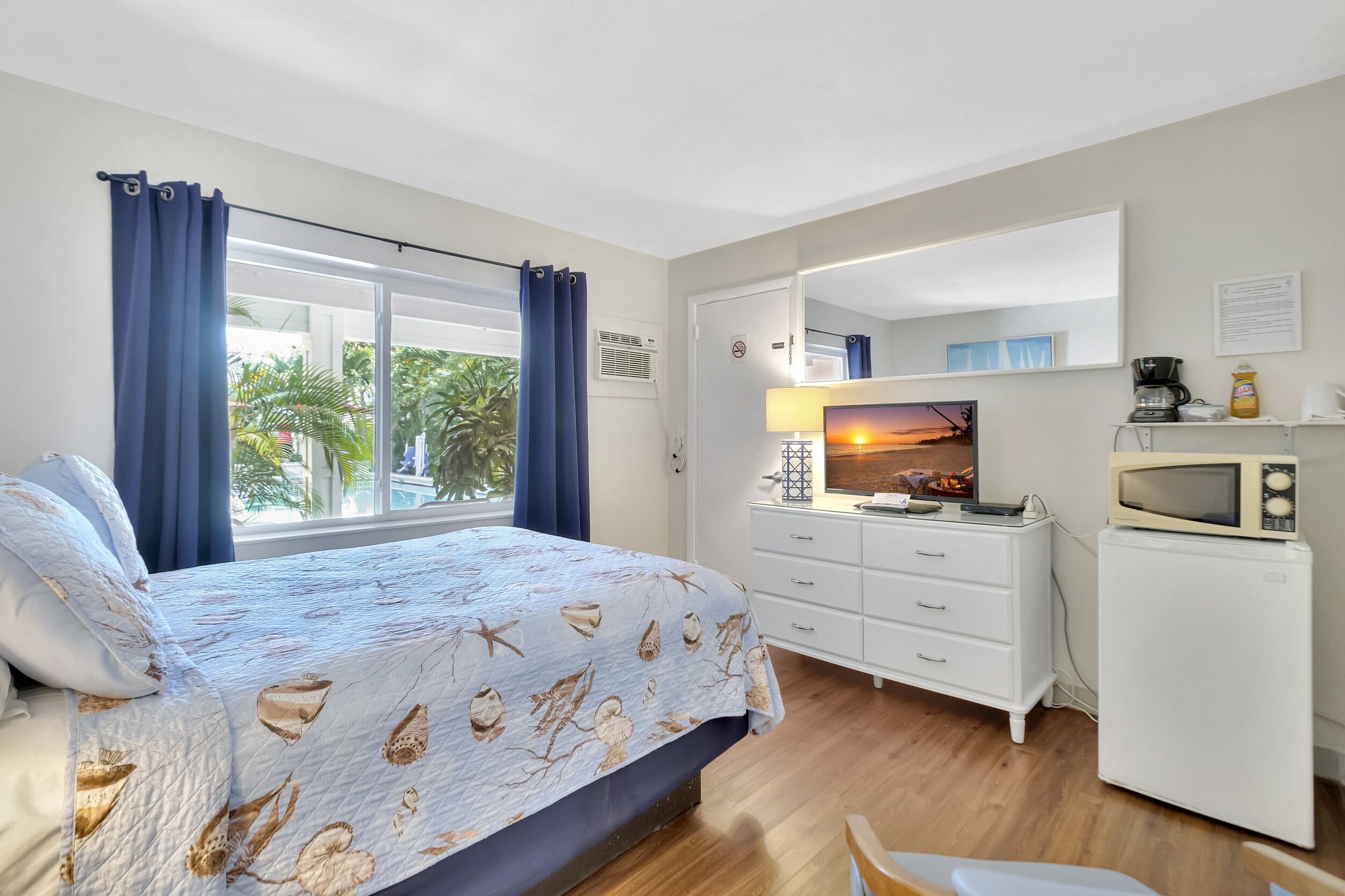 Une chambre à coucher comprenant un lit, une commode, un four à micro-ondes, une télévision et une fenêtre avec des rideaux.