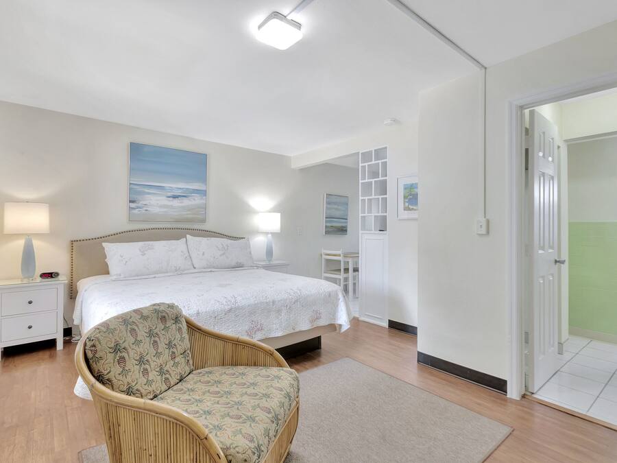 A bedroom with a bed, bedside tables, a chair, and a view of a green outdoor area.