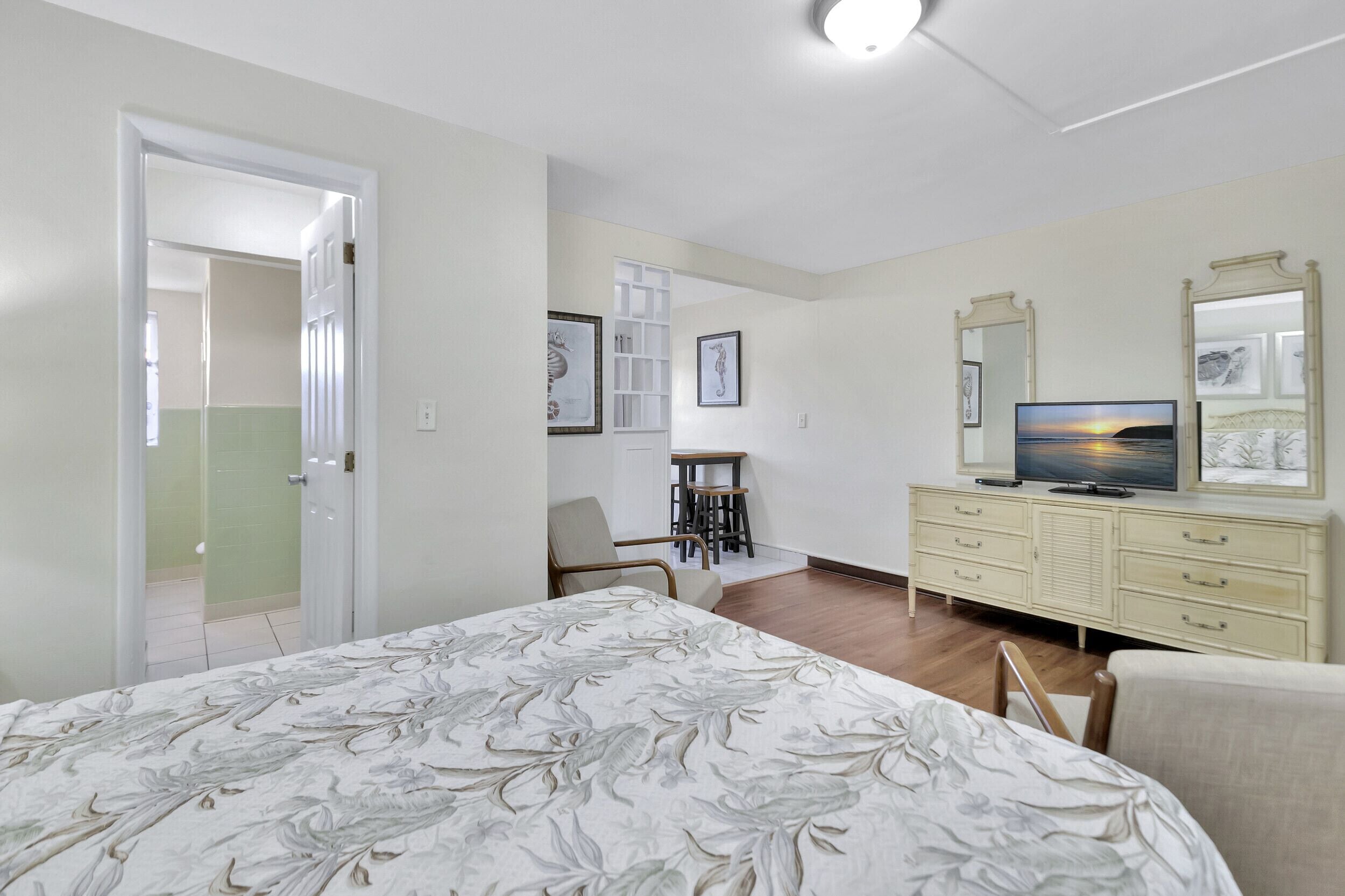 Un dormitorio con cama, televisor, cómoda y una silla.