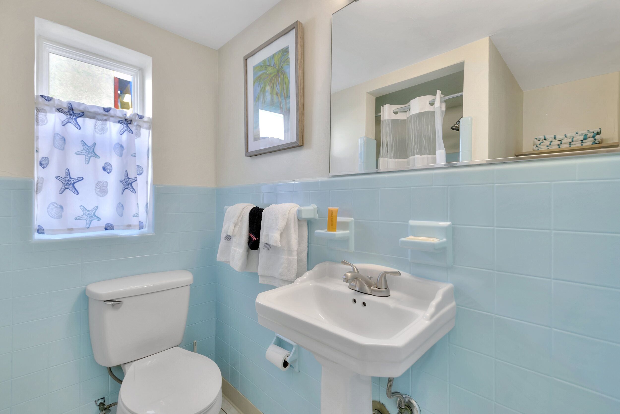 A bathroom with a toilet, sink, and window with a starfish curtain.