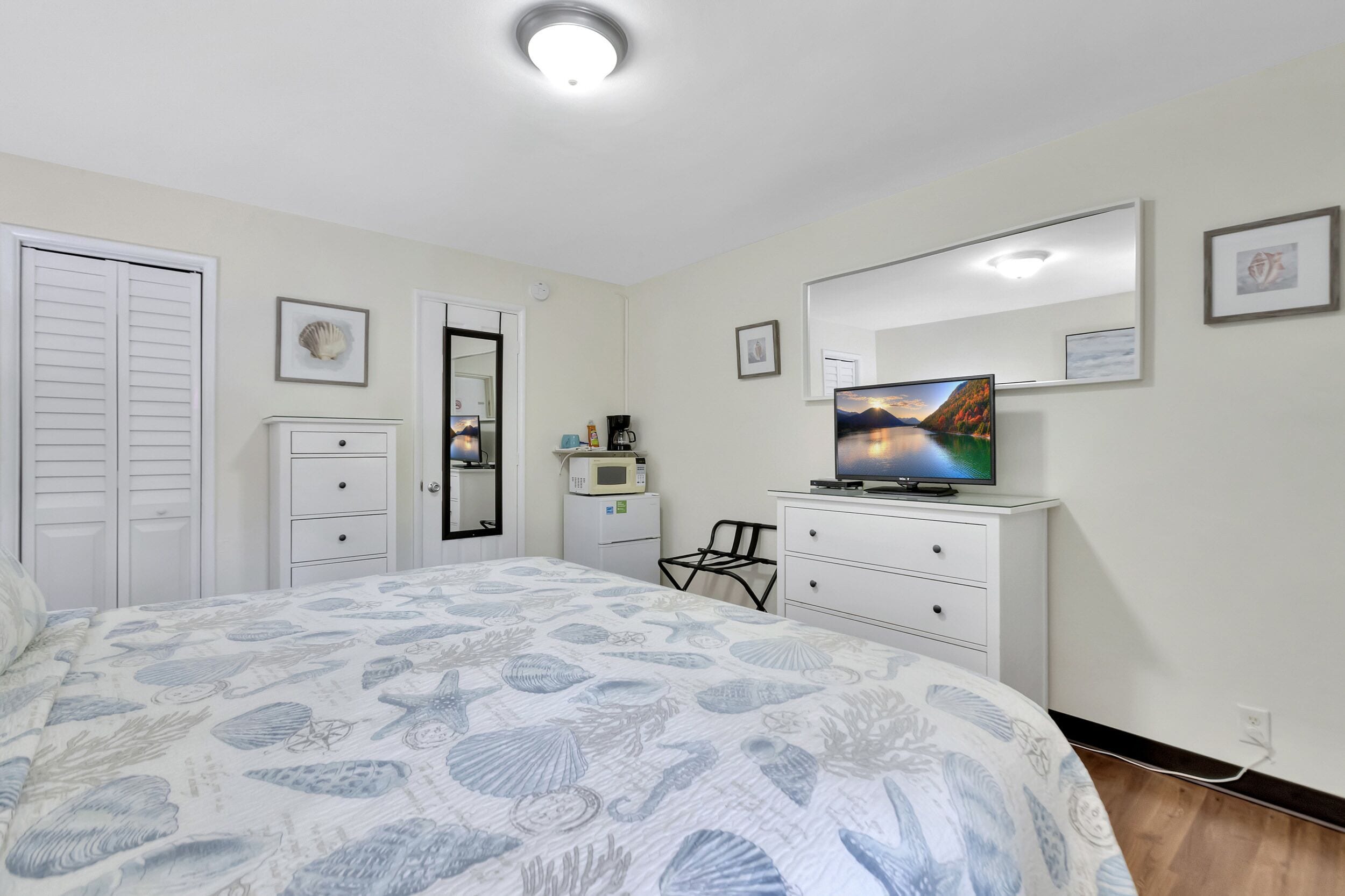 A bedroom with a bed, a television, a dresser, a chair, a microwave, and a door.