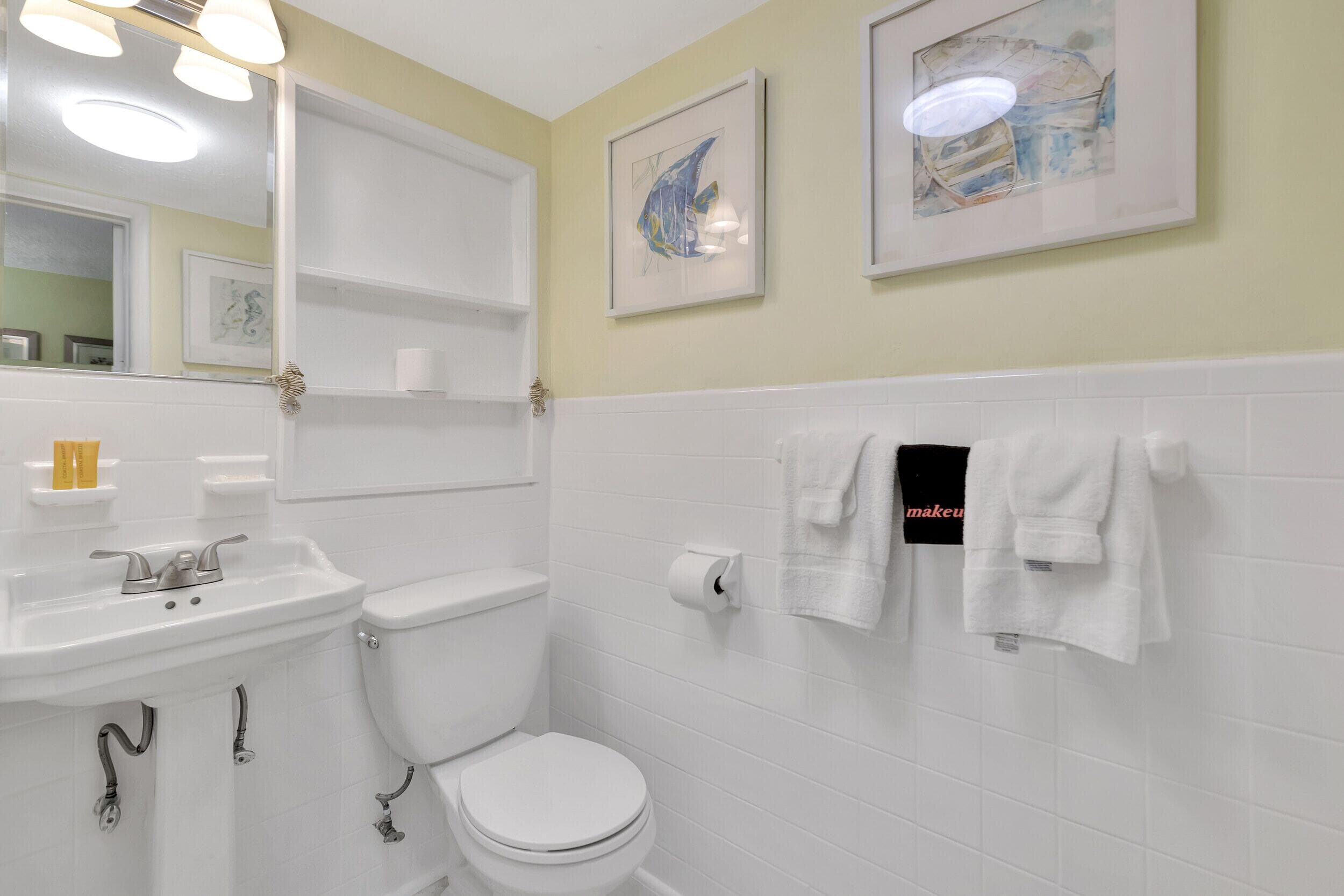 A bathroom with a white sink, toilet, and towel rack. There are two framed pictures on the wall.