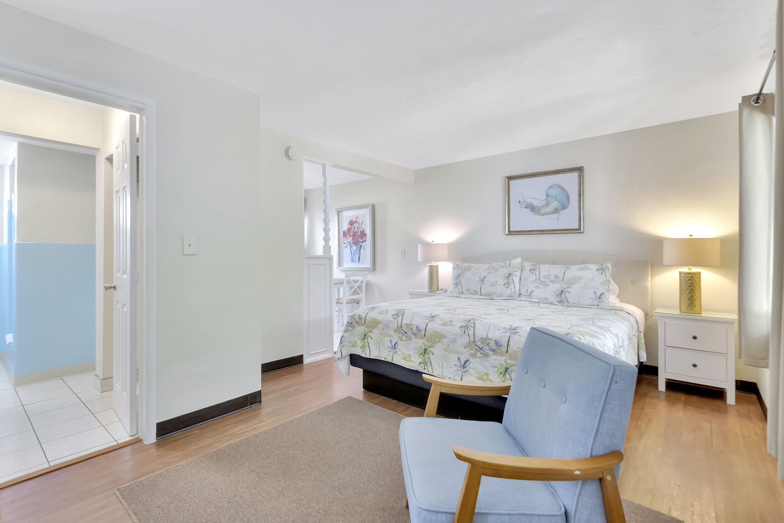 A bedroom with a bed, a chair, a nightstand, and a wall-mounted lamp.