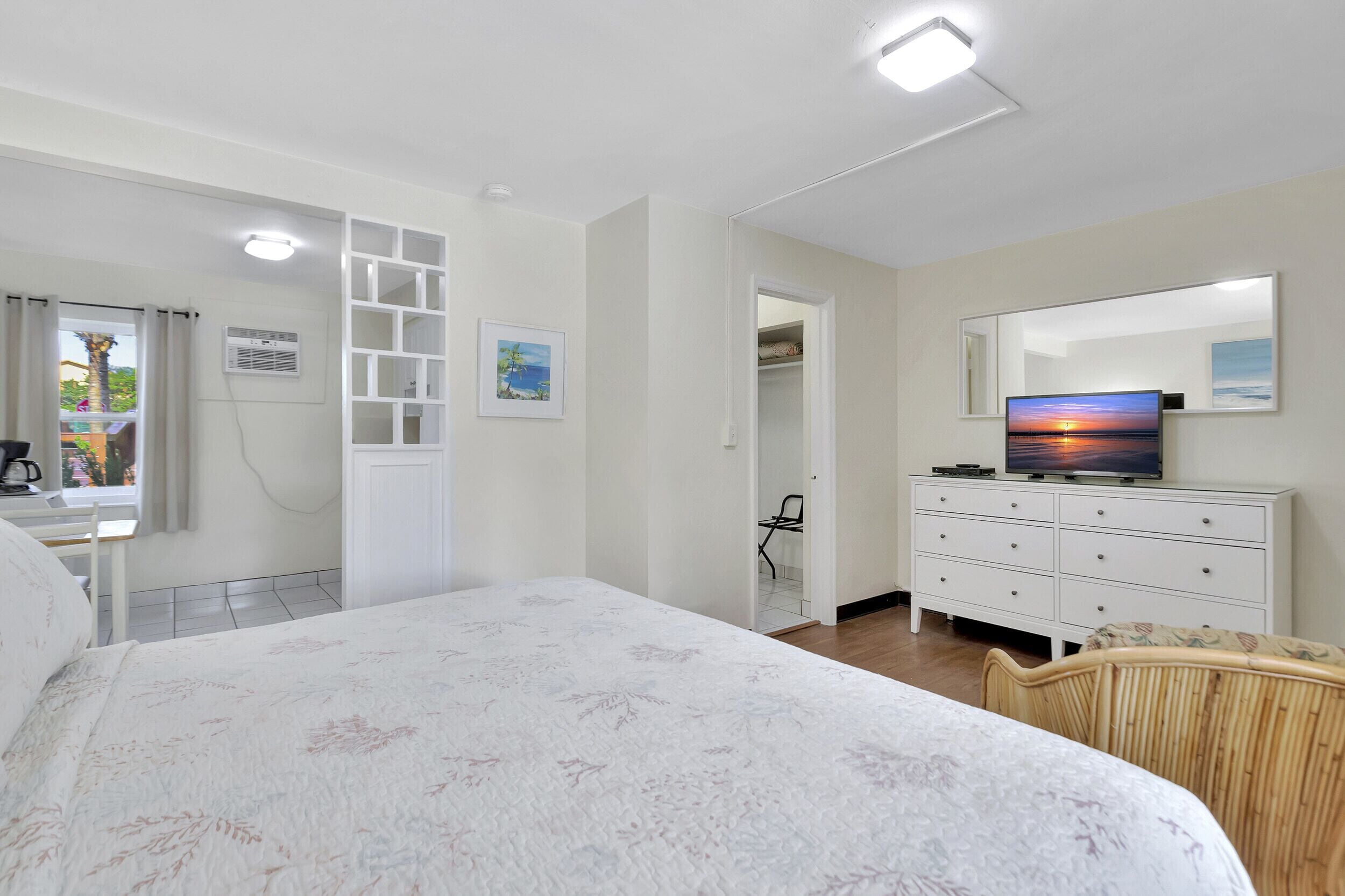 A bedroom with a bed, a dresser, a TV, and a window with curtains.