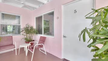 A room with pink walls, a white door marked with the number 5, a potted plant, and two chairs.