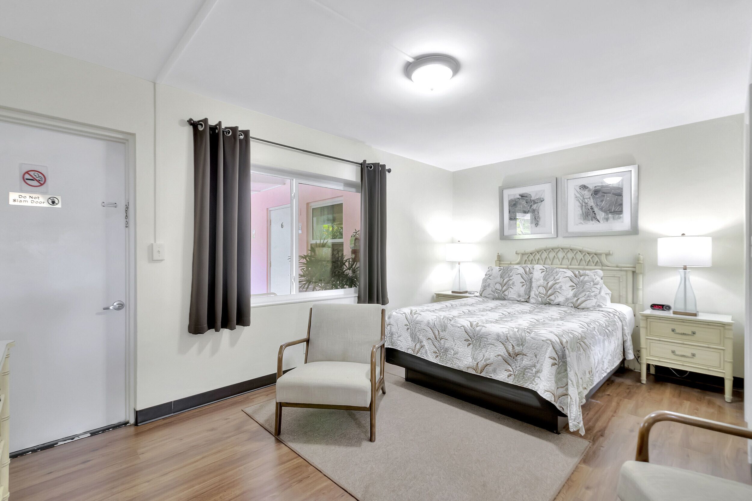 Une chambre à coucher avec un lit, des tables de chevet, une chaise, une fenêtre avec des rideaux et une porte.