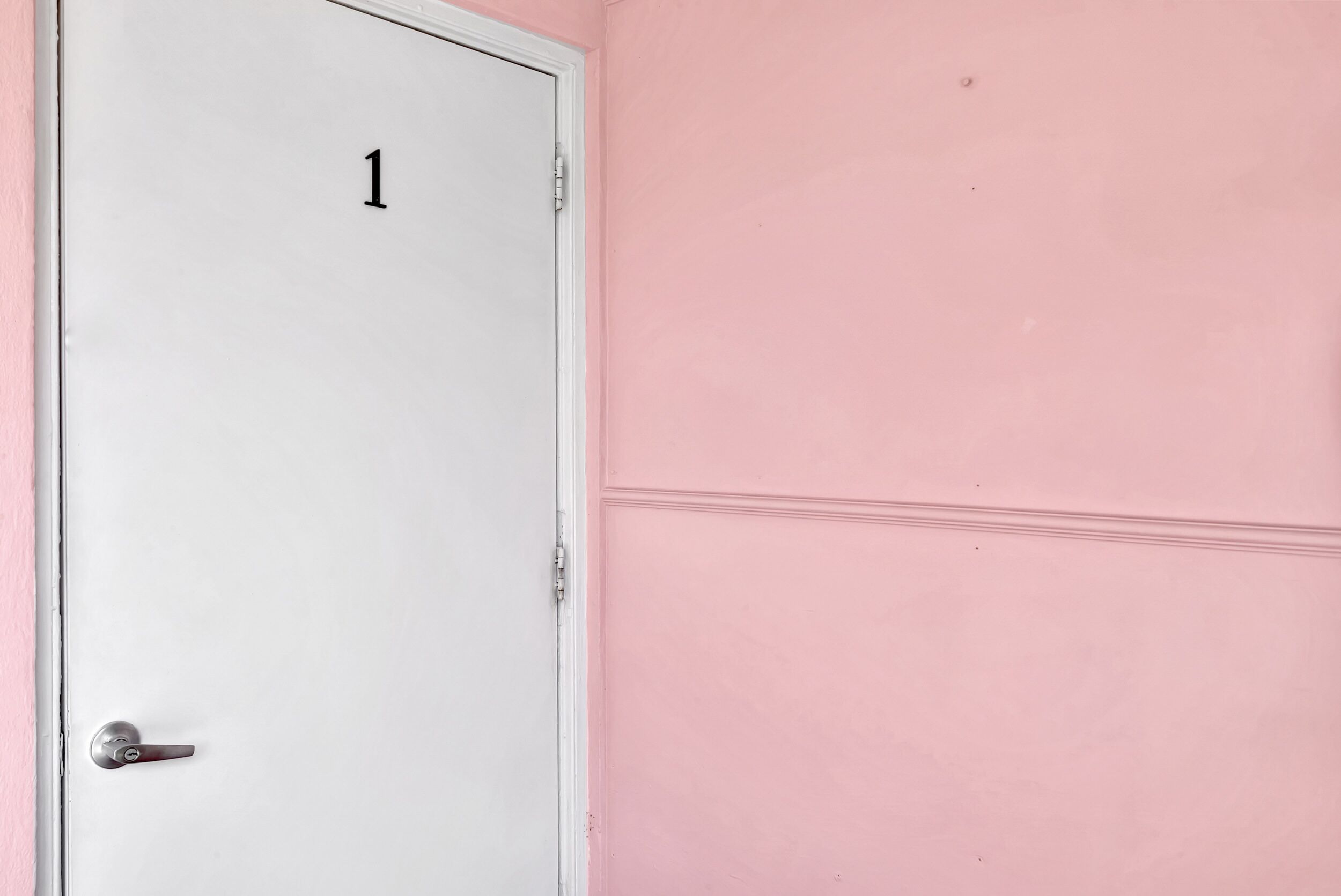 A white door with the number 1 on it, next to a pink wall.
