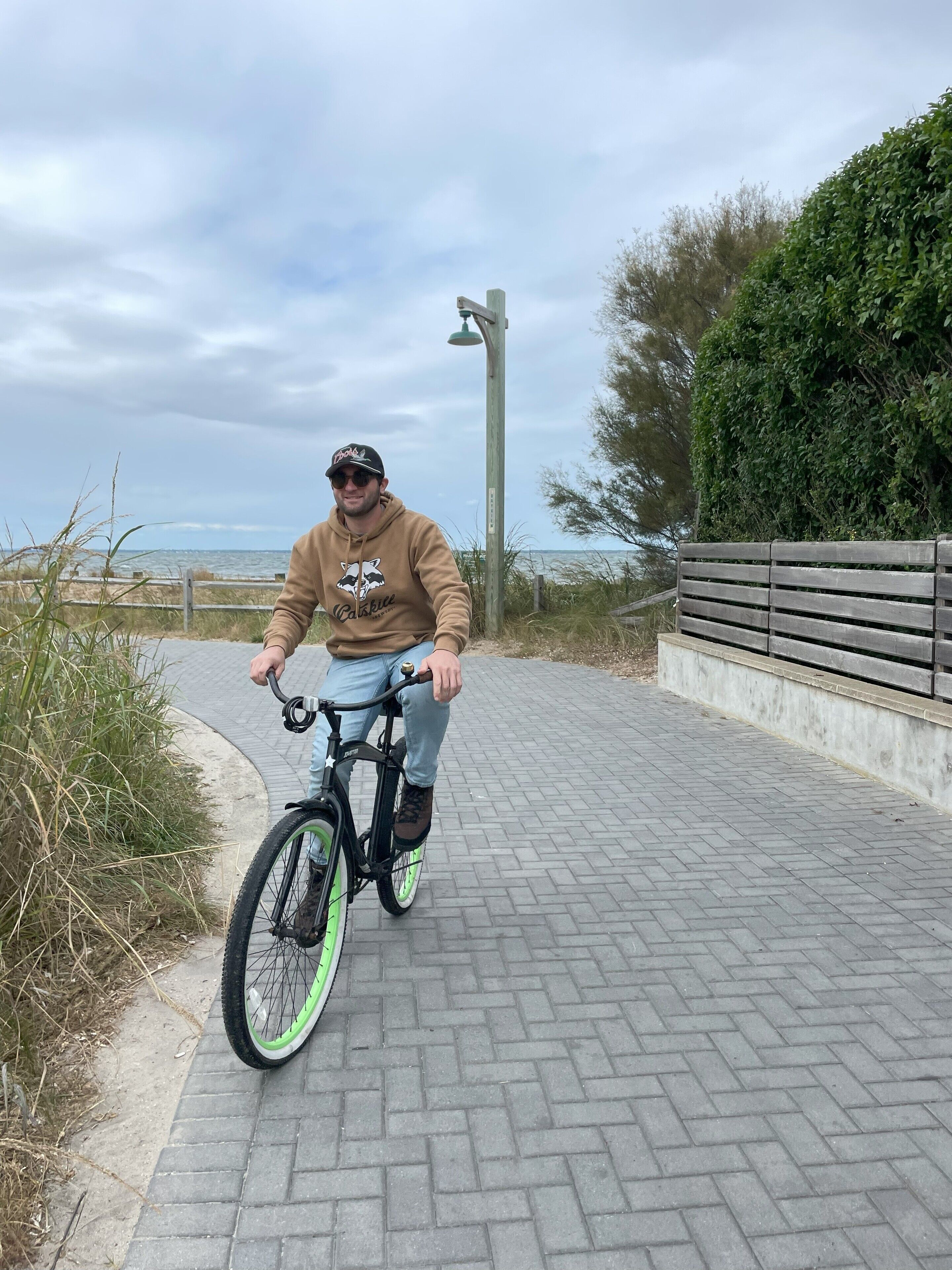 A person riding a bicycle on a paved path with a wooden fence and greenery on one side.