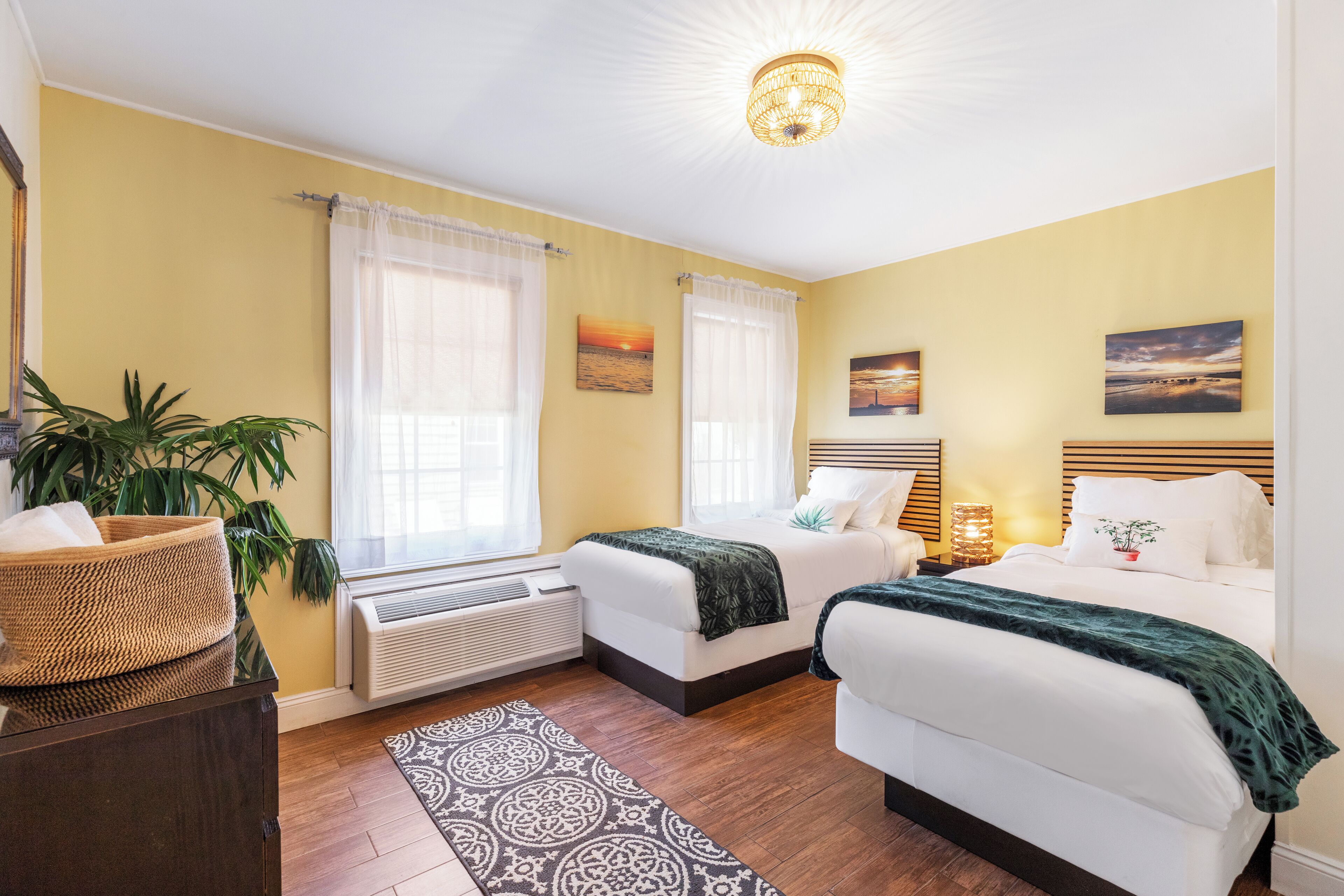 A hotel room with two beds, a large window with sheer curtains, a patterned rug, and a ceiling light fixture.