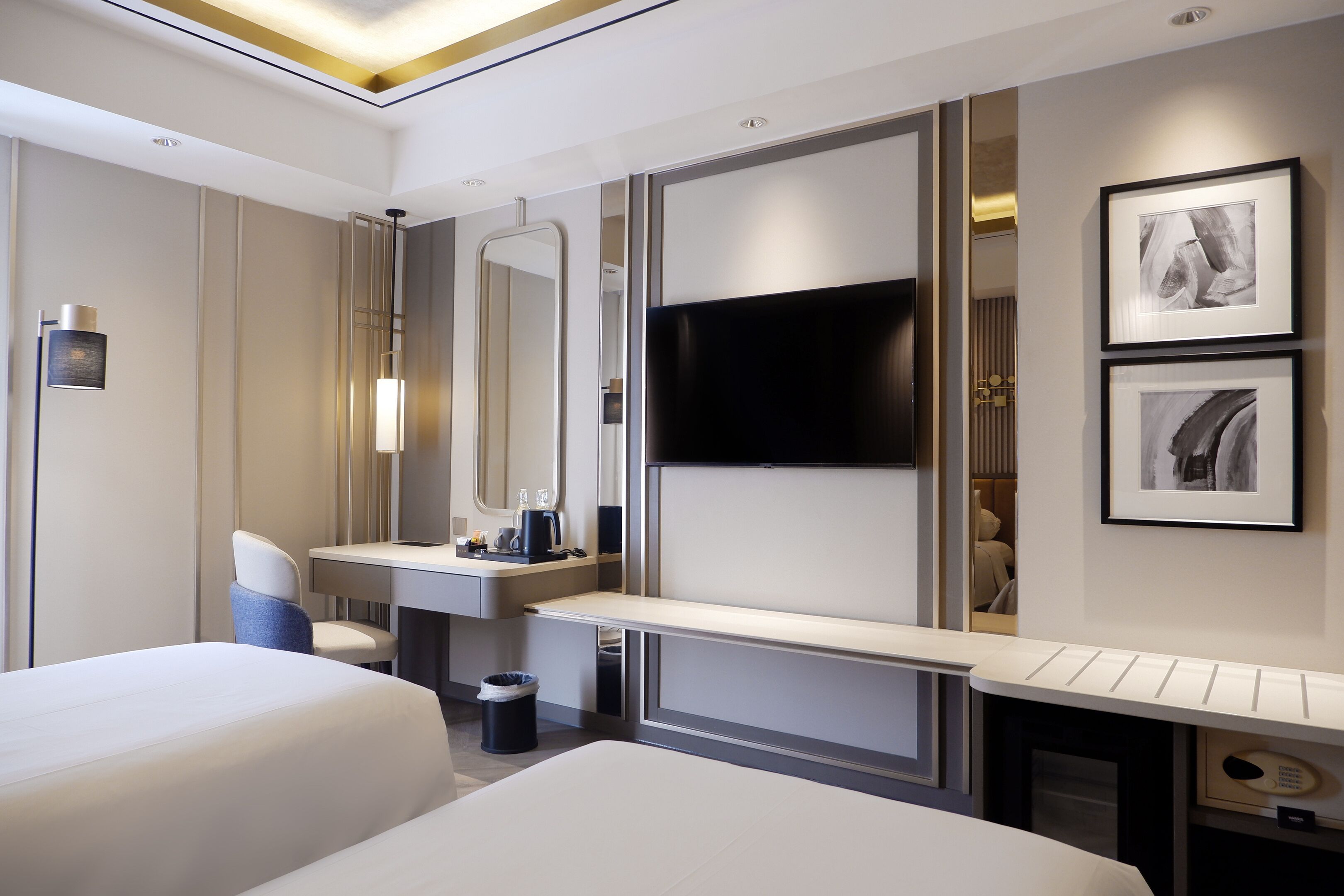 Habitación de hotel moderna con dos camas, un espejo grande, un televisor de pantalla plana, un escritorio y un cubo de basura pequeño.