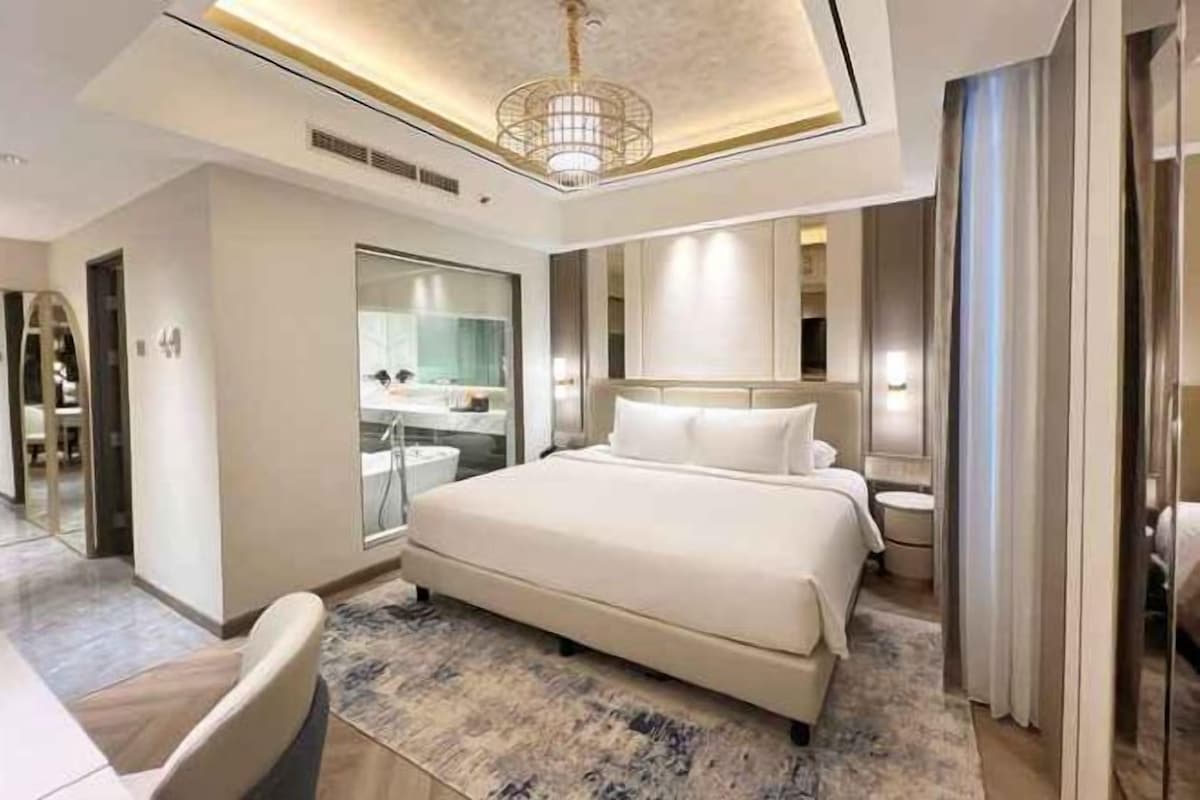 Una habitación de hotel moderna con una cama grande, una zona de estar y un baño con ducha de vidrio.