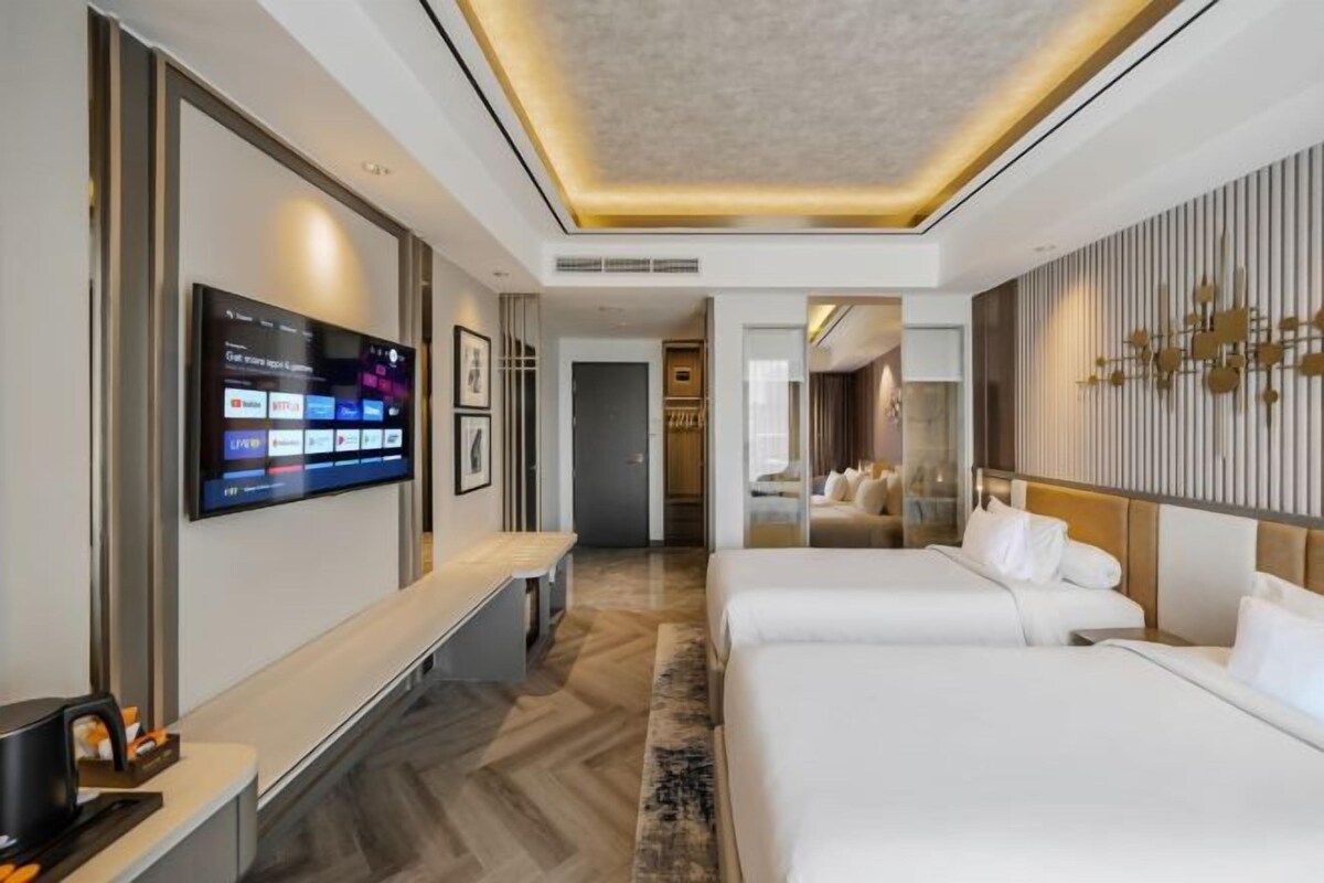 Una habitación de hotel moderna con un televisor de pantalla plana grande, dos camas, una zona de estar y un diseño de pared elegante.