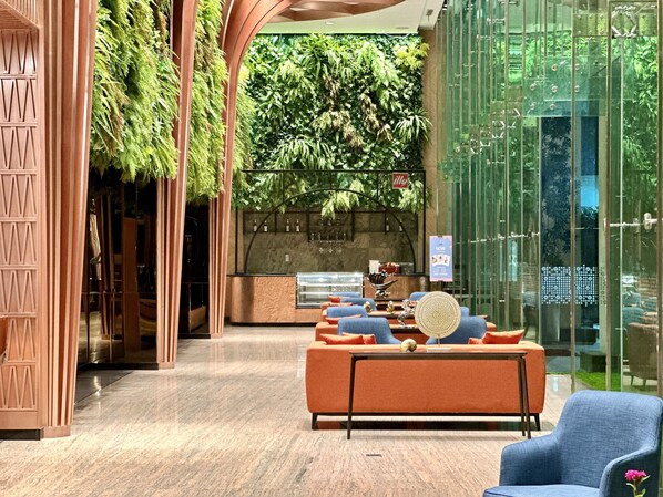 Un vestíbulo moderno con zona de estar, mostrador de recepción y pared verde con plantas.