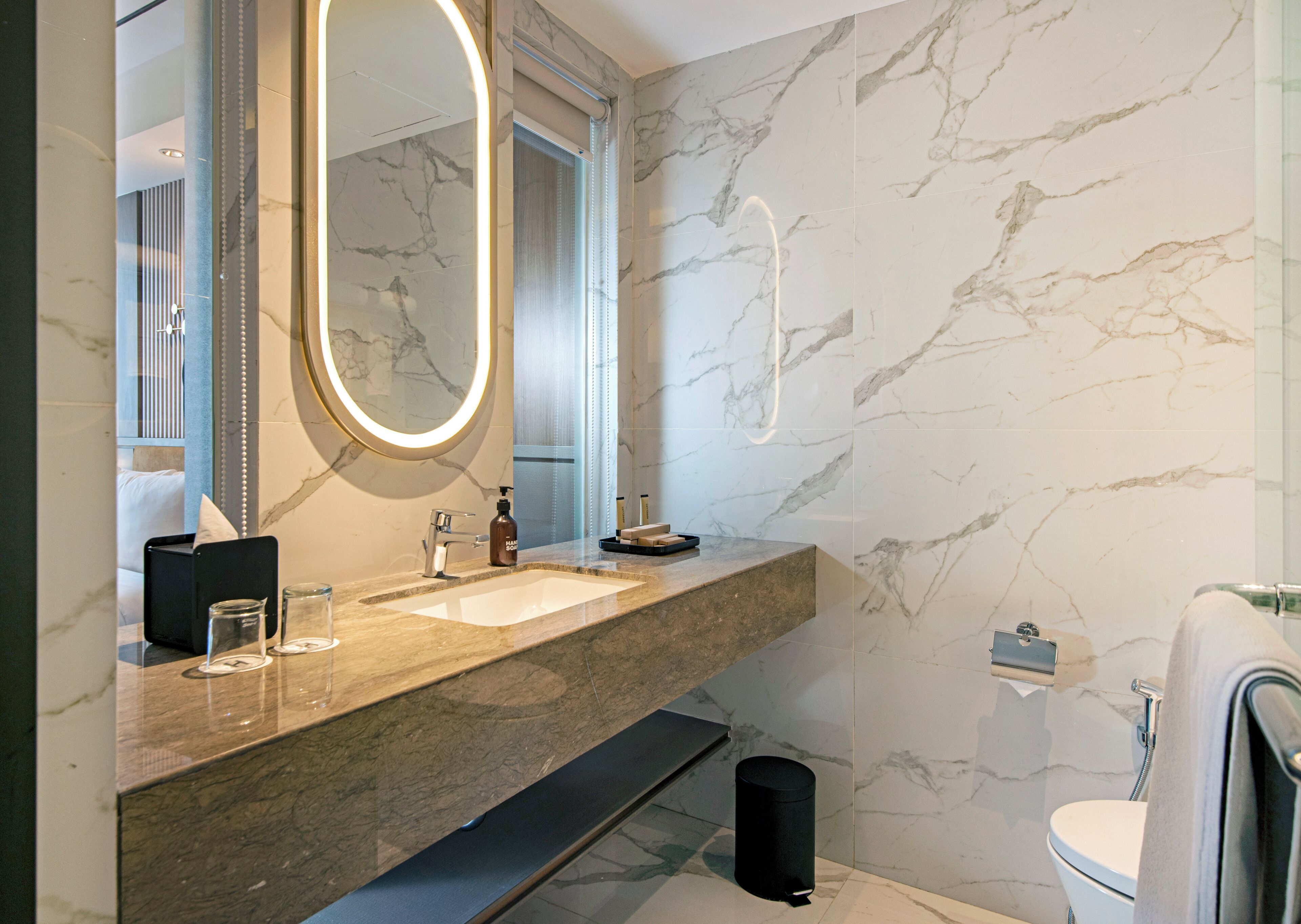 A modern bathroom with a marble backsplash, a large mirror, a sink, and a toilet.