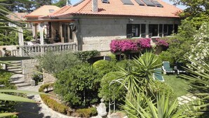 Un bâtiment en pierre, doté d’un toit en tuiles, entouré d’une végétation luxuriante et de plantes en fleurs.