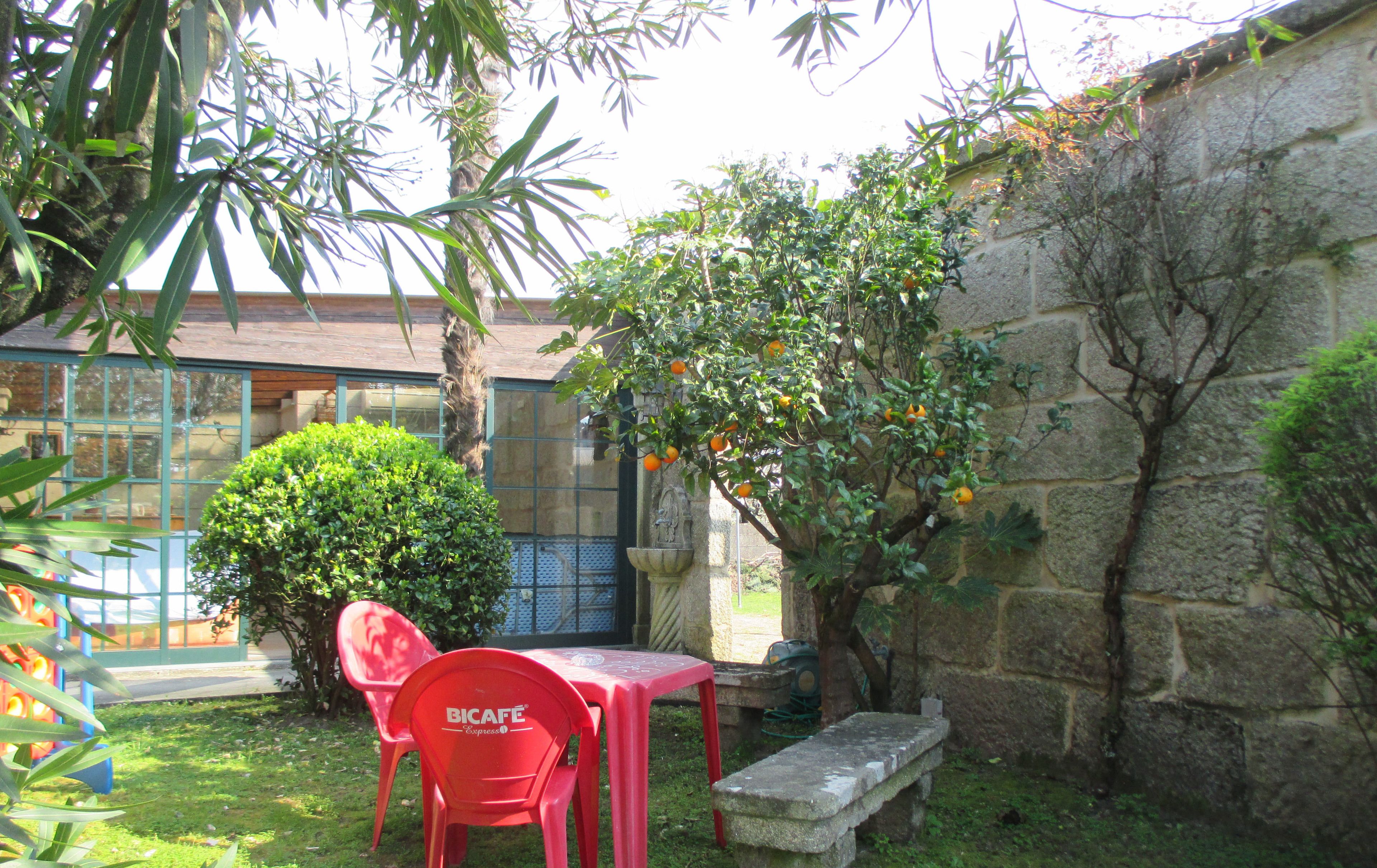 Un patio con una mesa y sillas rojas de BICAFE Express, un muro de piedra y un árbol con naranjas.