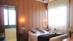 Une chambre d’hôtel avec deux lits, des boiseries, un lustre, des lampes de chevet, un téléphone et un vase avec des fleurs.