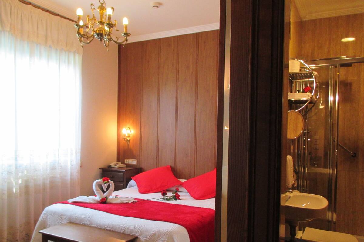 Ein Hotelzimmer mit Bett, einer Kandelaber, einer Wandlampe, einem Nachttisch und einem Badezimmer mit Dusche und Waschbecken.