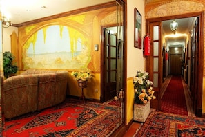 Um saguão de hotel com um grande mural, um sofá, um tapete estampado e um carpete vermelho.