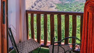 Un balcón con vistas a montañas, dos sillas y barandal de madera.