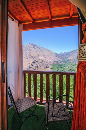 A balcony with a view of mountains, two chairs, and a wooden railing.