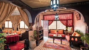 A traditional Moroccan interior with ornate arches, a patterned rug, and a variety of furnishings including sofas and a table. - Atlas Prestige (Asni)