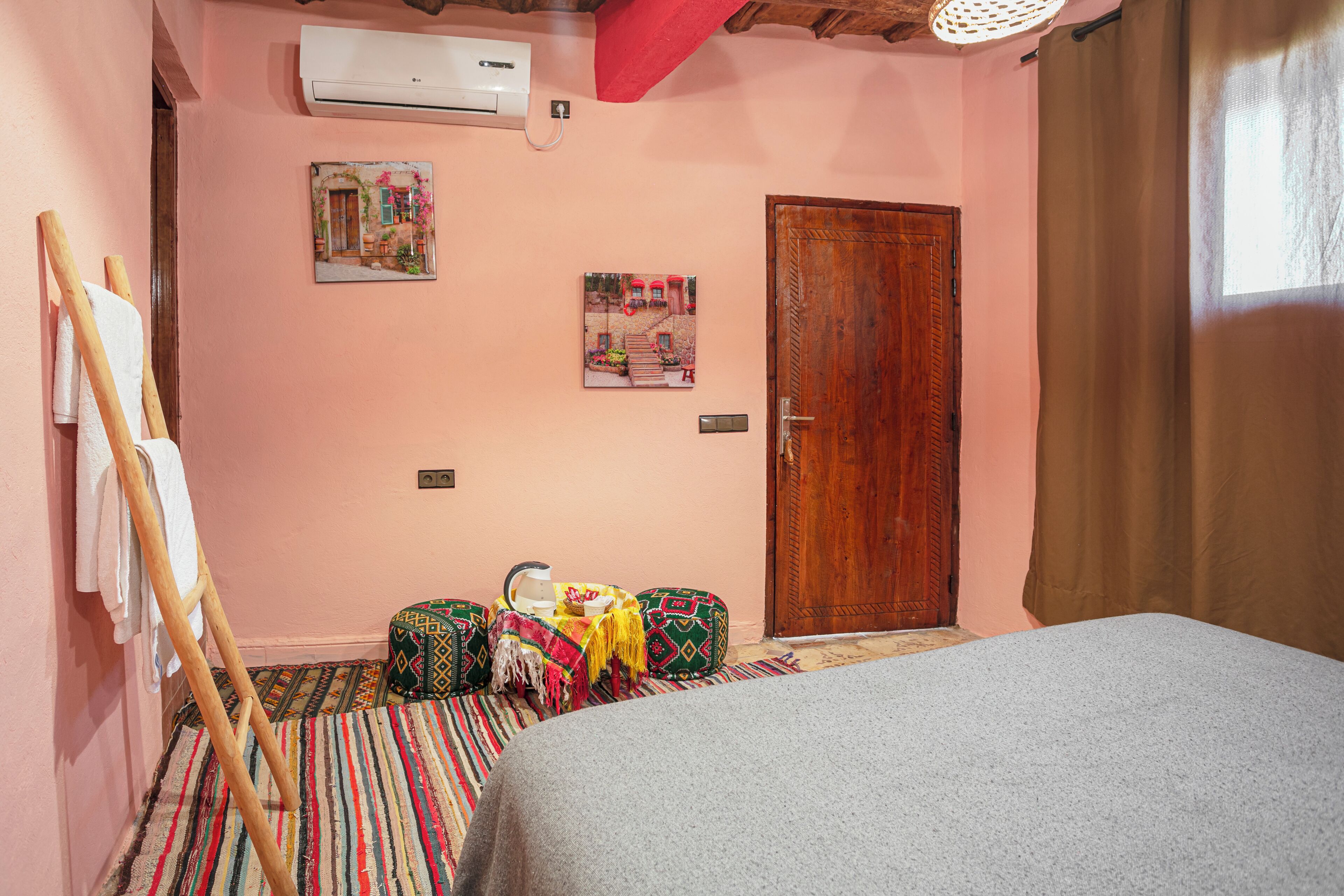 A bedroom with a bed, a wooden door, a wall-mounted air conditioner, and a colorful striped carpet.