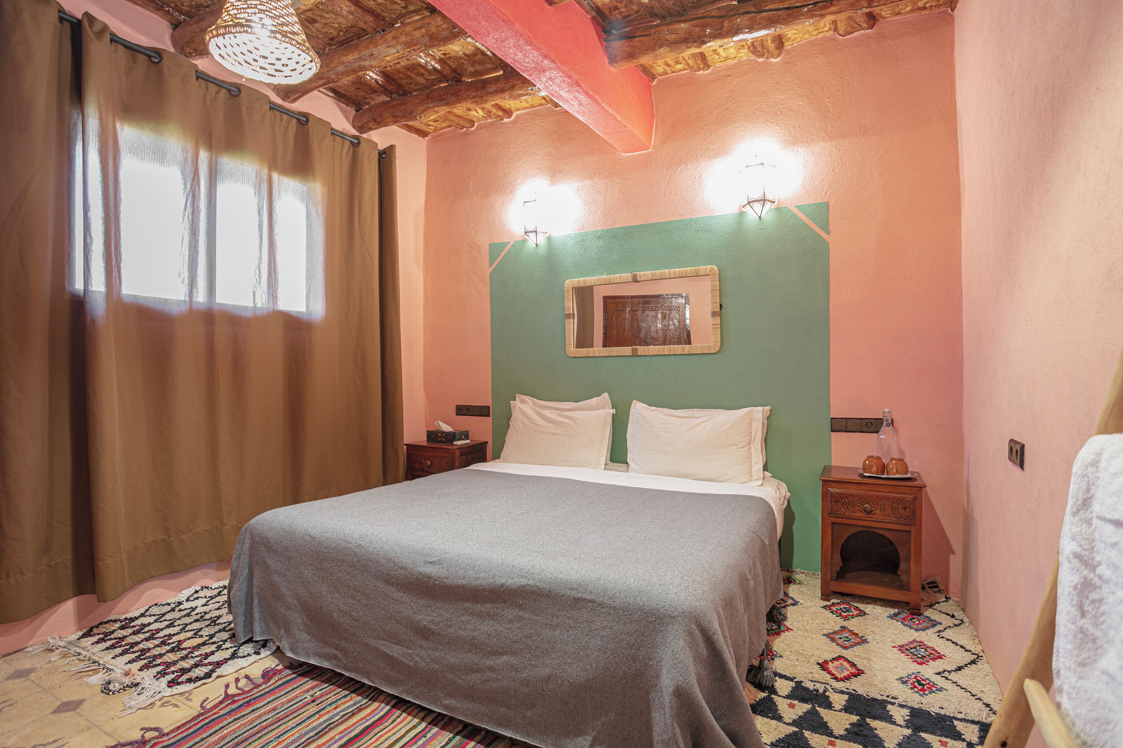 A bedroom with a bed, a nightstand, a wall-mounted light, and a patterned rug.