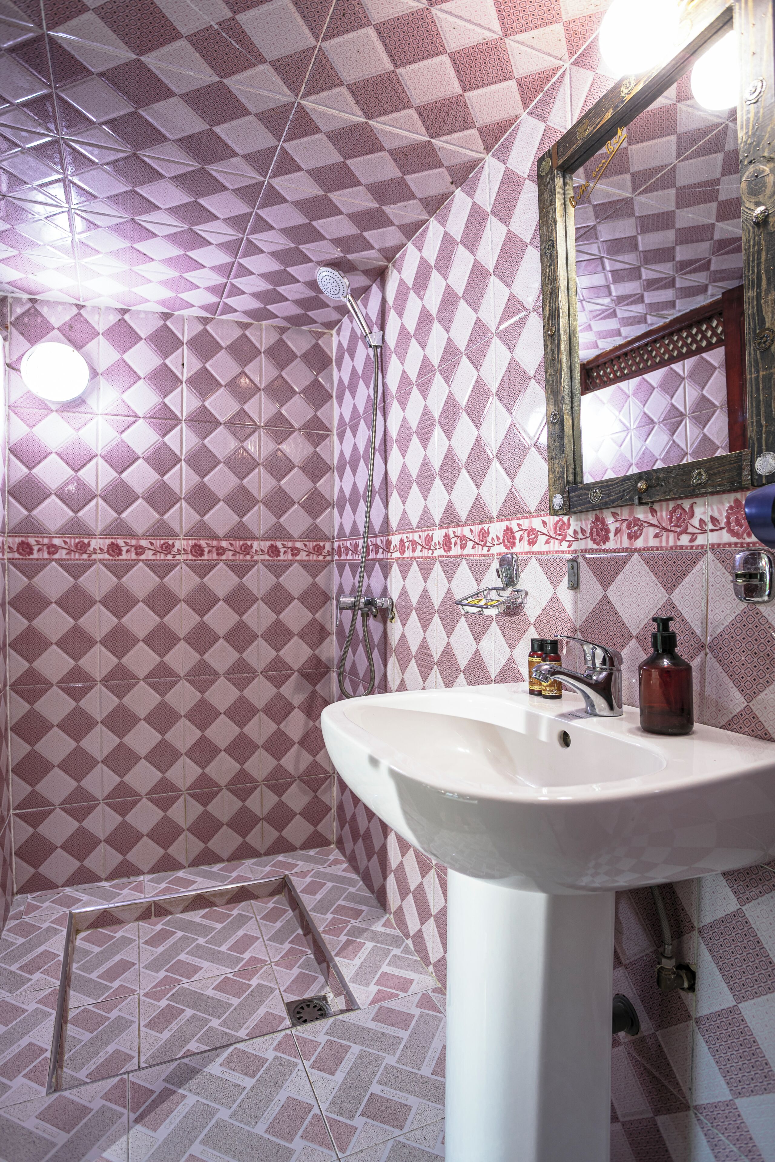 A bathroom with a geometric patterned tile design, a white sink, a mirror, and a shower area.