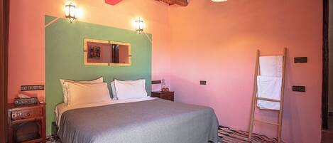 Un dormitorio con una cama, una escalera de madera, una mesita con taza y plato, y un tapete estampado.