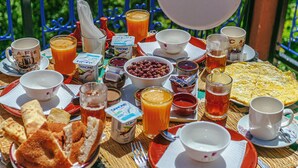A table set with breakfast items, including bread, eggs, and beverages, on a balcony with a view of greenery.