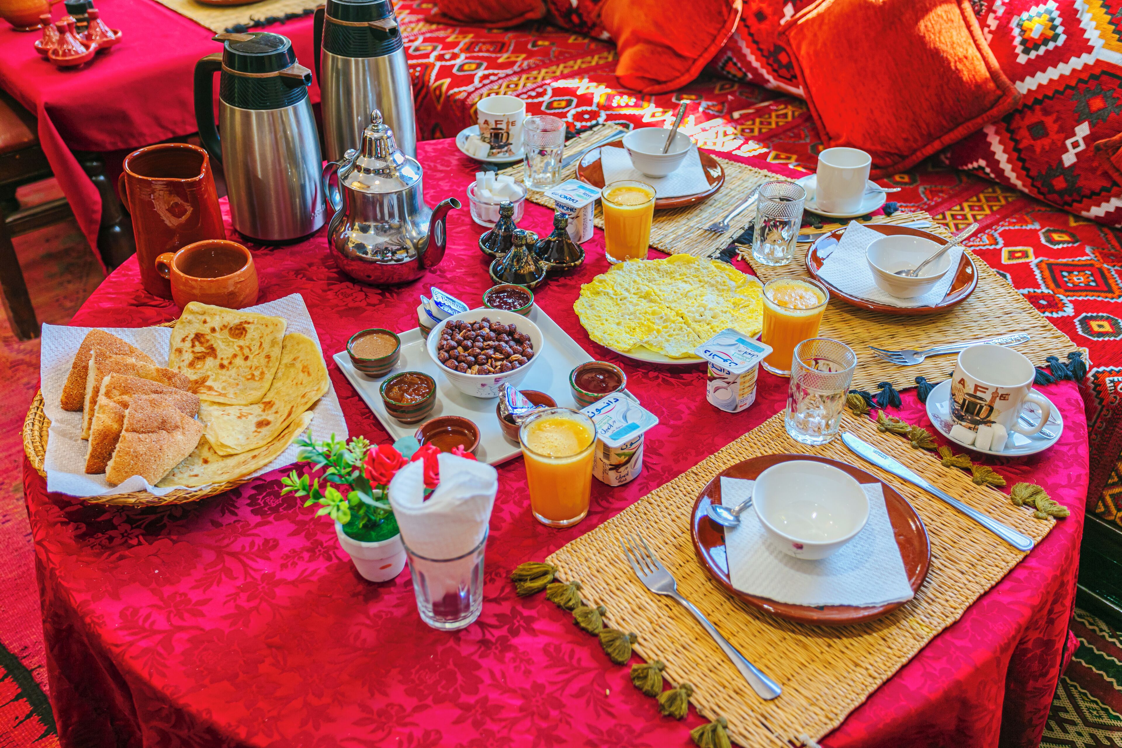 Una mesa de desayuno con diversos alimentos y bebidas, sobre un mantel rojo.