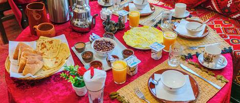 Una mesa de desayuno con diversos alimentos y bebidas, sobre un mantel rojo.