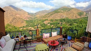 A balcony with a view of a mountainous landscape, furnished with a sofa, chairs, and a table.