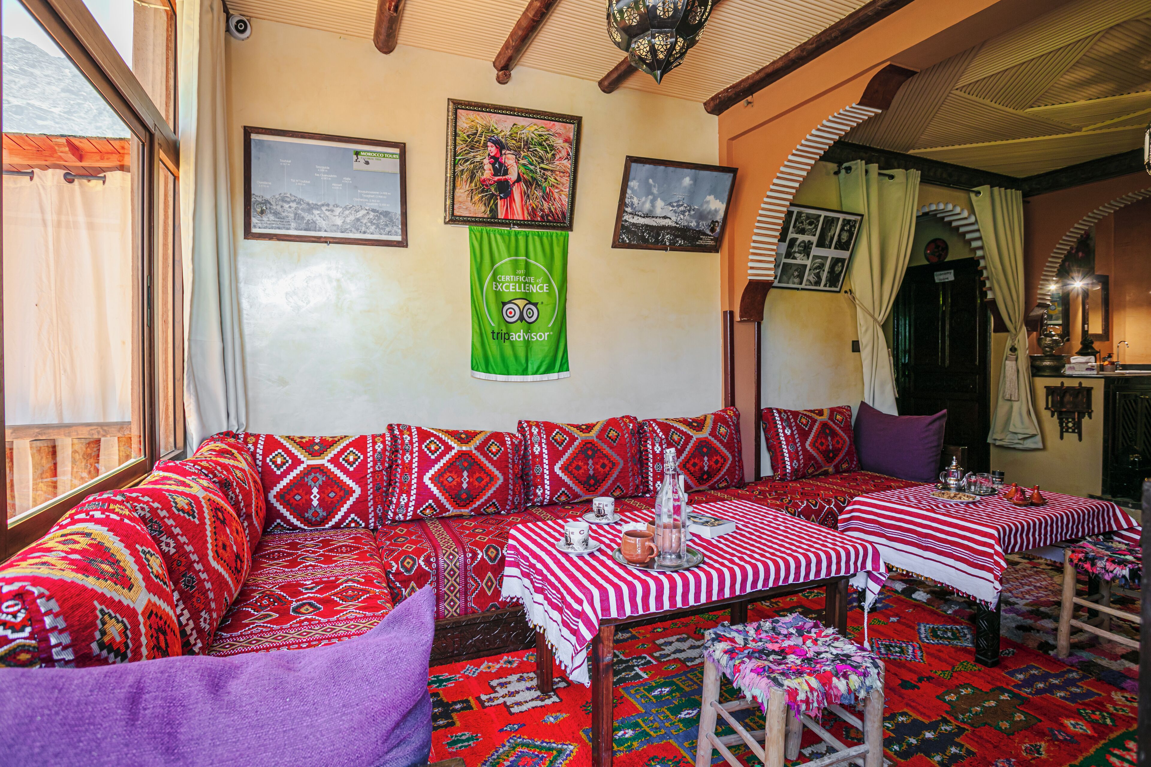 A traditional room with a sofa, two tables with striped tablecloths, and a view of mountains through a window.