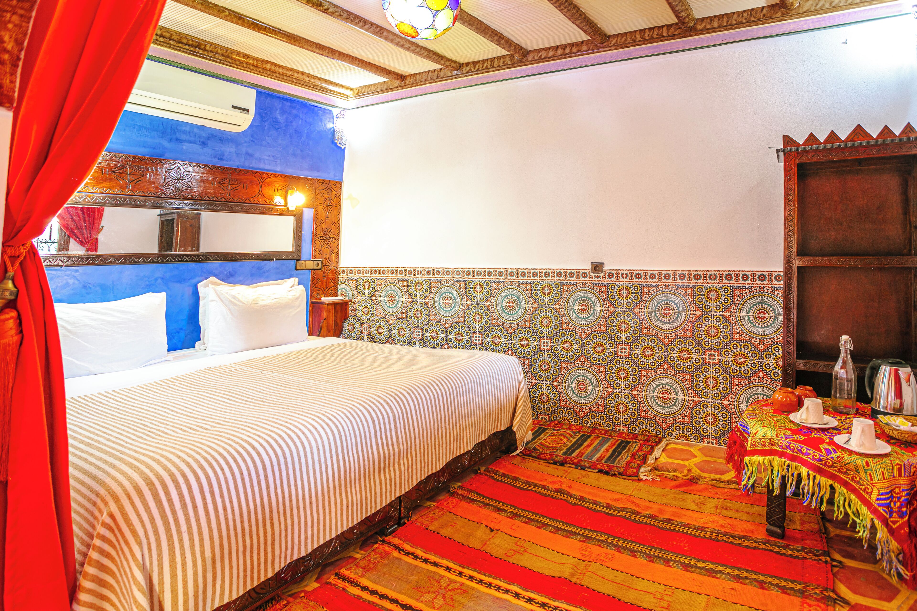 A room with a bed, a table with a teapot, and a patterned wall.