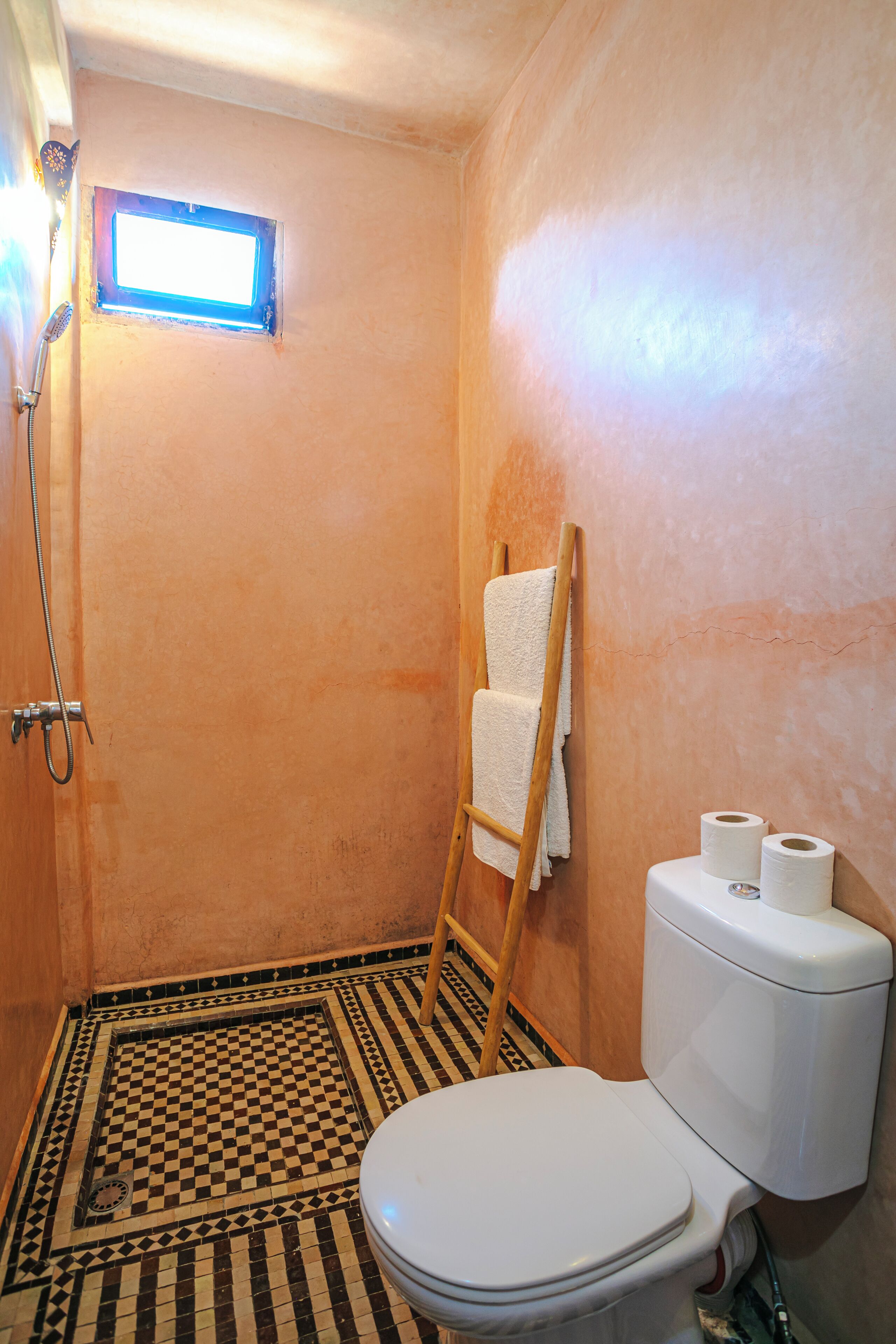 A bathroom with a checkered floor, a white toilet, a shower, and a towel rack.