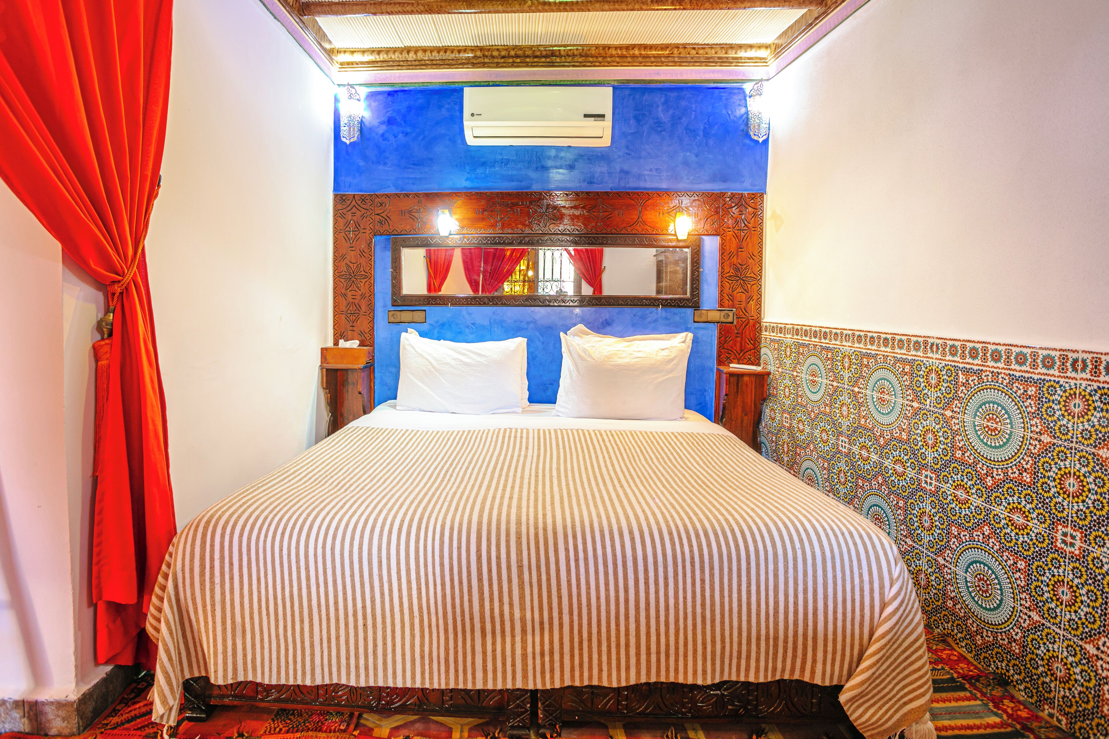 A hotel room with a bed, a mirror, a red curtain, and patterned walls.