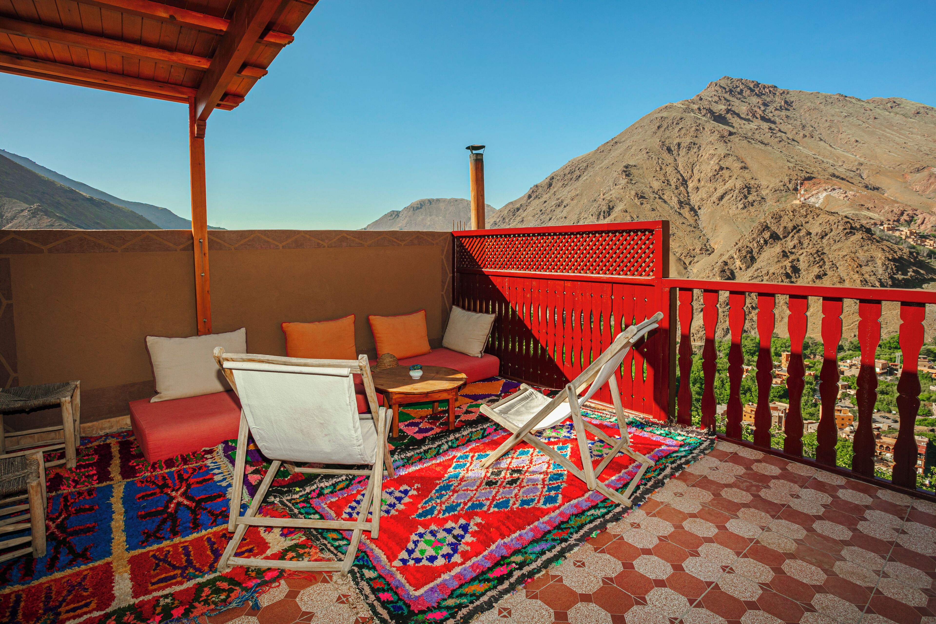 Ein Balkon mit roter Geländer, einem gemusterten Teppich und einer Sitzecke mit Tisch und Stühlen.