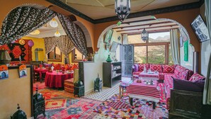 A room with a patterned rug, a sofa, a table, and a view of the outdoors. - Atlas Prestige (Asni)