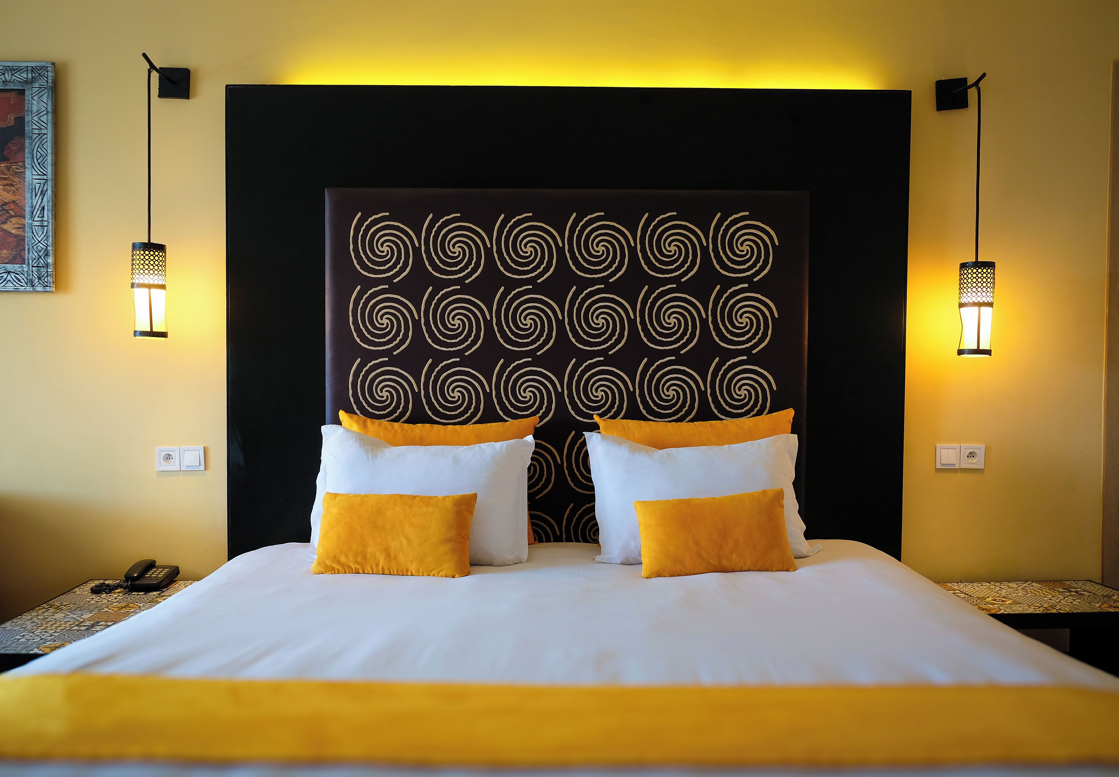 A hotel room with a large bed, two bedside lamps, a patterned headboard, and a telephone on the nightstand.