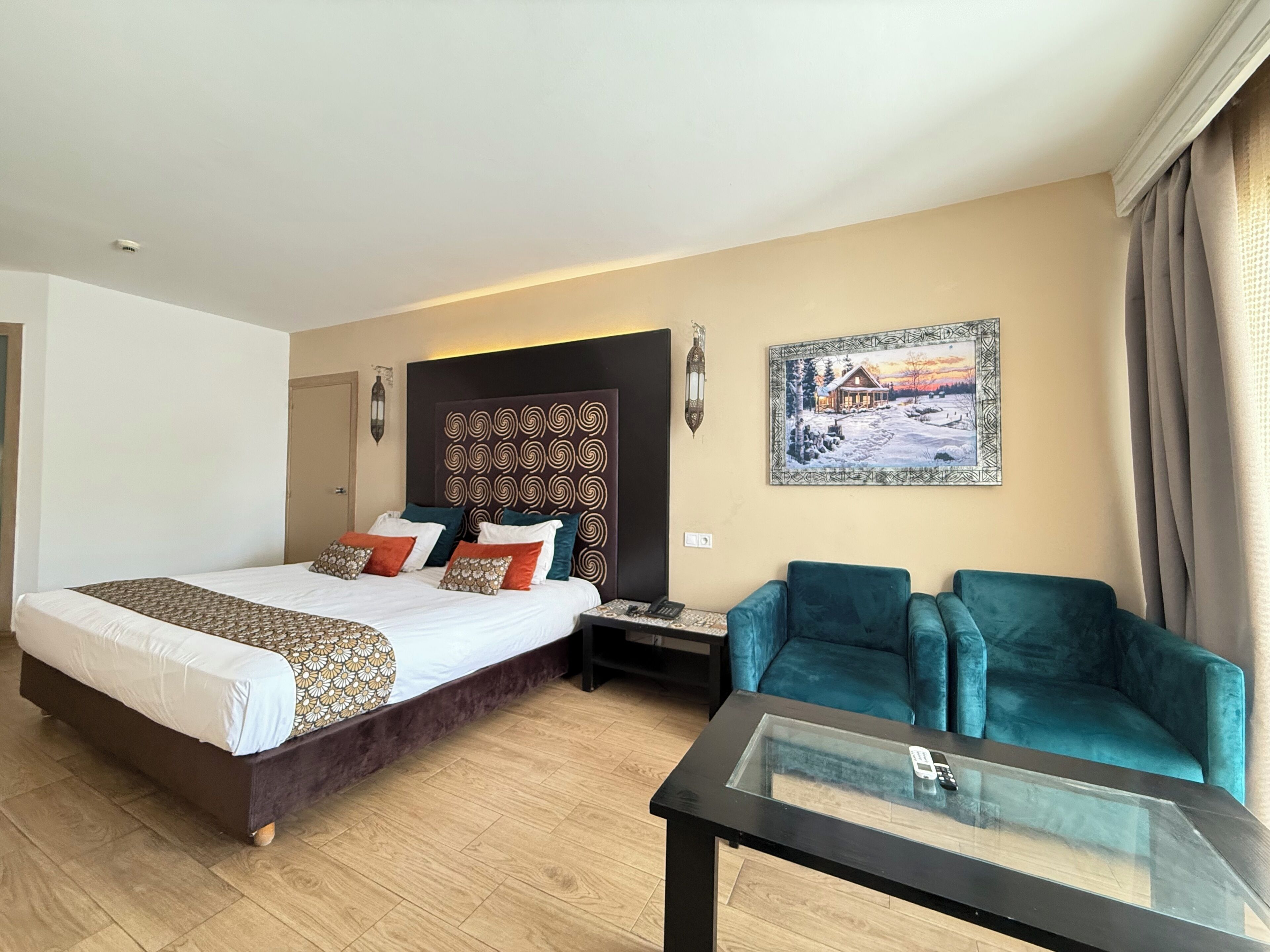 A hotel room with a large bed, a desk, two chairs, and a painting on the wall.