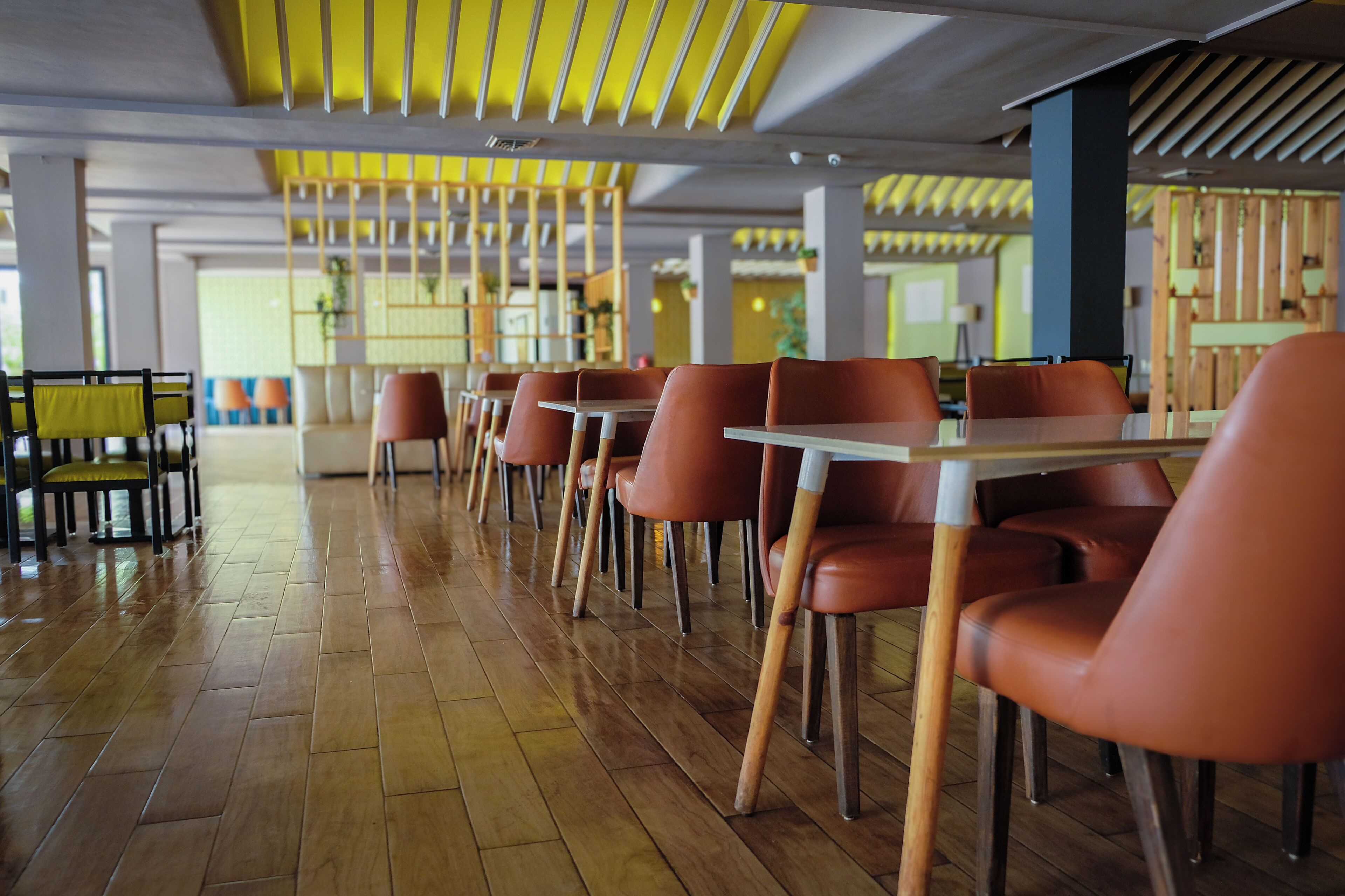 Un interior de restaurante moderno con suelo de madera, sillas color naranja y detalles en el techo color amarillo.
