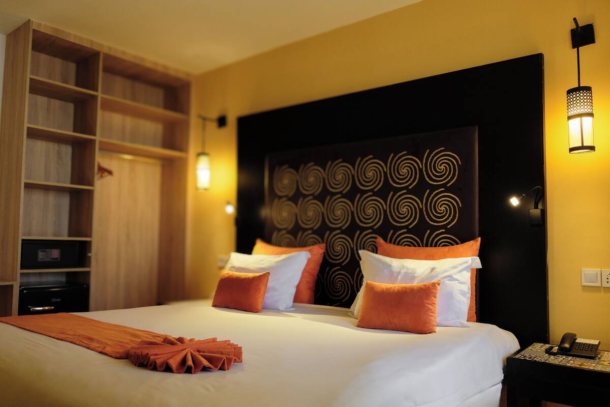 Quarto de hotel com cama, mesa de cabeceira com telefone, estante de livros e cabeceira com design espiral.