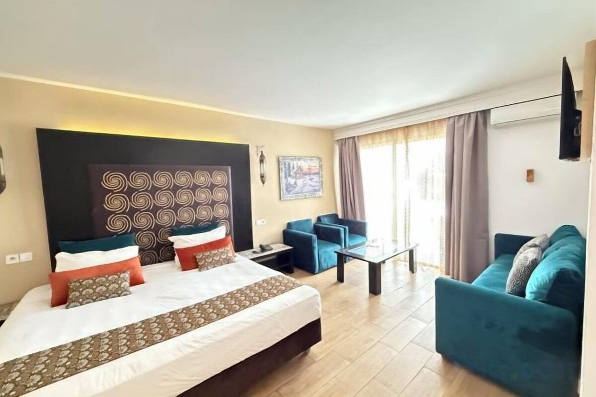 Ein Hotelzimmer mit einem großen Bett, zwei Sofas, einem kleinen Tisch und Blick ins Freie.