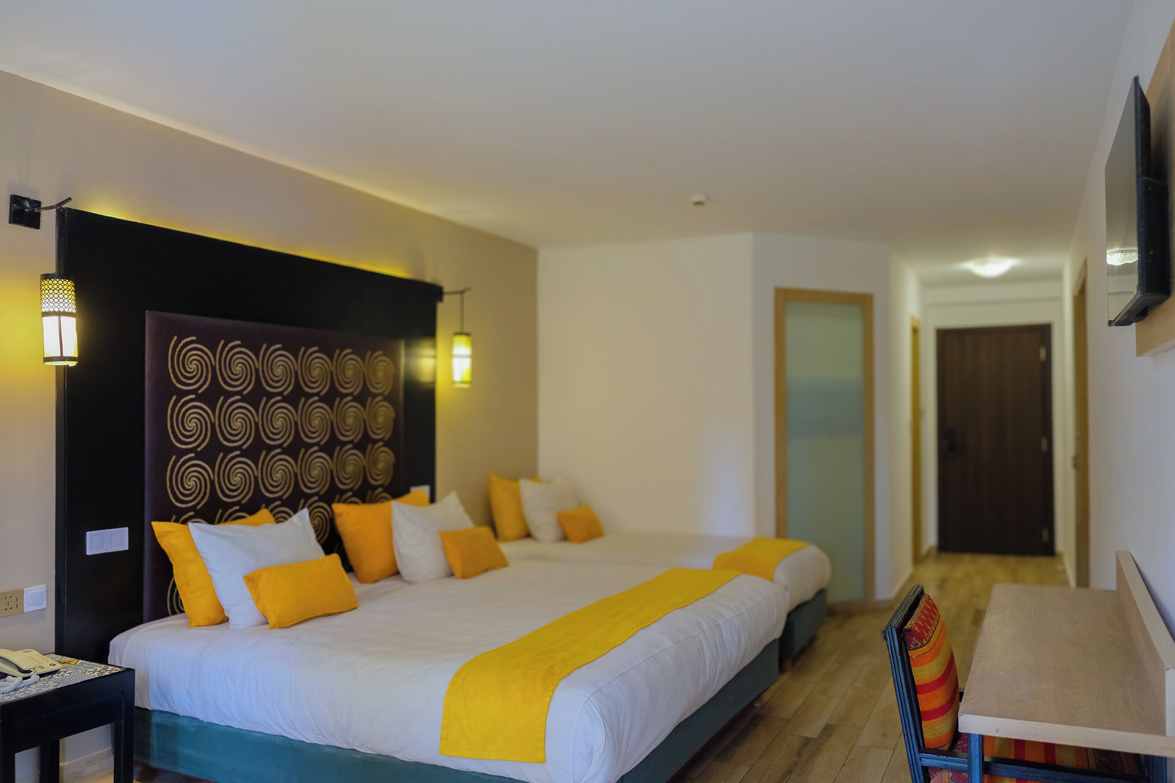 Una habitación de hotel con una cama grande, mesitas de noche, un escritorio y un televisor montado en la pared.