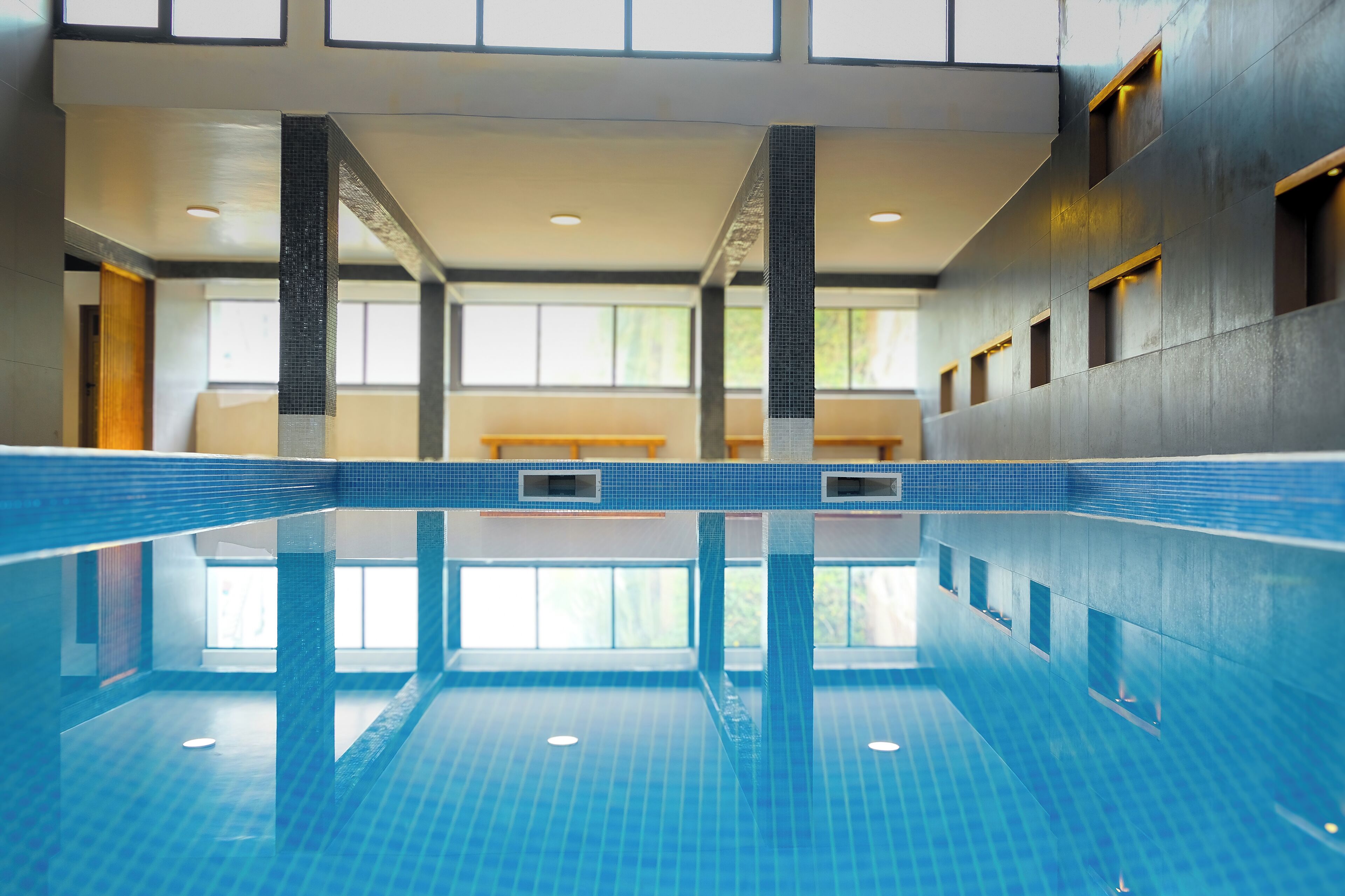 An indoor swimming pool with clear blue tiles, a tiled floor, and a view of the outside through large windows.